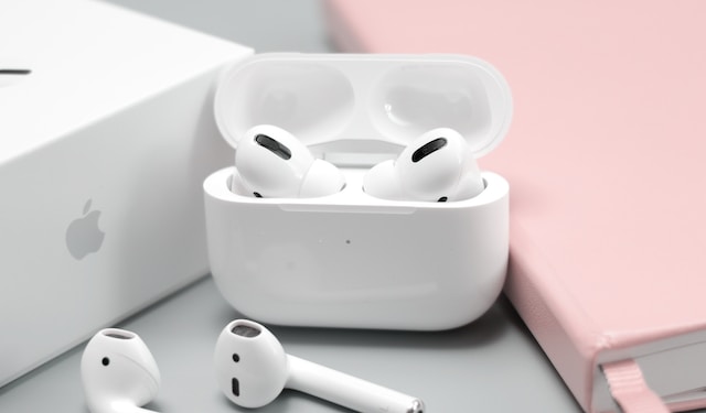A photo of apples airpods in a airpod cover and airpod box and pink notebook